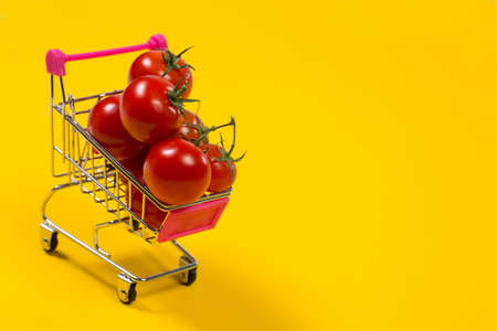 Cherry tomatoes and shopping cart on yellow backgroundの写真素材