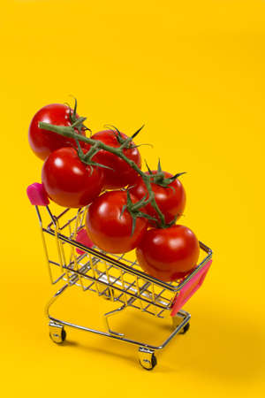 Cherry tomatoes and shopping cart on yellow backgroundの写真素材