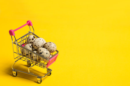 Small quail eggs in a shopping cart on a yellow background, healthy foodの写真素材