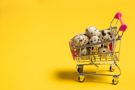 Small quail eggs in a shopping cart on a yellow background, healthy foodの写真素材