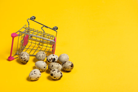 Small quail eggs in a shopping cart on a yellow background, healthy foodの写真素材