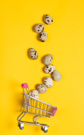Small quail eggs in a shopping cart on a yellow background, healthy foodの写真素材
