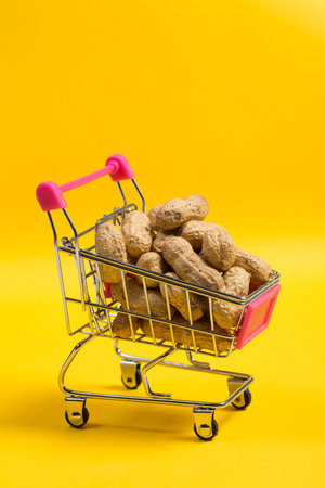 Peanuts in shell in a shopping cart on a yellow background, healthy foodの写真素材
