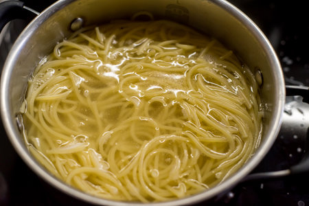 Long spaghetti boiling in pot. Water surrounds noodles bubbling steadily. Steam rises above surface. Cooking process visible. Progress evident. Meal preparation ongoing. Kitchen atmosphere captured.の写真素材