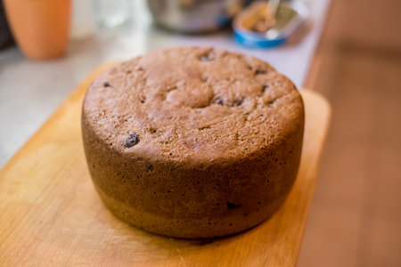 Large cherry cake placed upright on wooden board, golden crust shows baked texture, small cracks, scattered spots. Fresh sponge cools gently, ready slicing, sharing over warm homemade gathering.の写真素材
