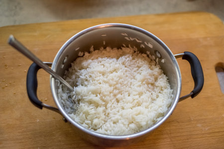 Cooked rice rests inside pot with spoon inserted gently. Steam lingers softly. Simple kitchen atmosphere suggests warmth, flavor, texture, stillness, balance, light, care, presence, comfort.の写真素材