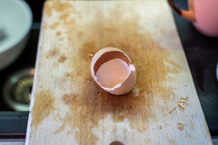 Eggshell lies on cutting board. Water drops remain nearby. Wooden surface shows trace. Sink visible...