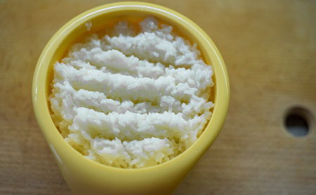 Cooked rice in round yellow container sits on wooden board, indicating portion presentation for serving or further preparation within culinary workflow context.の写真素材