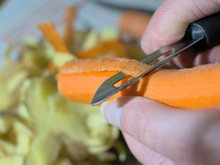 Carrot peeling with a peeler, above a pile of potato peelings
