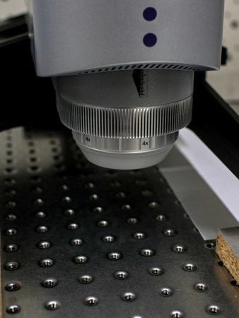 Slightly blurred profilometer head above a steel plate with threaded holes