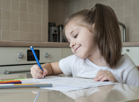 Cute little girl  drawing with colorful pens at  kitchen table at home. Creative kid. Girl doing homework at home.の写真素材