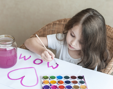 Child making homemade greeting card. A little girl paints a heart  on a homemade greeting card as a gift for Mother Day. Traditional play concept. Arts and crafts conceptの写真素材