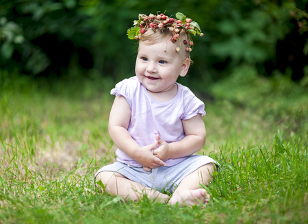 Cute baby girl with gold hair and wild strawberry crown, outdoor in gardenの写真素材