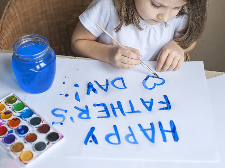 Child making homemade greeting card. Painted hand. A little girl paints a heart on a homemade greeting card as a gift for Father Day. Finger paint. Traditional play concept. Art and craft conceptの写真素材
