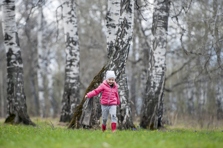 A little curly baby in a pink jacket and boots fun runs in the spring forest. The first flowers. Gentle symbol of spring. Caring for a new life. Earth day holiday concept. World Environment Dayの写真素材