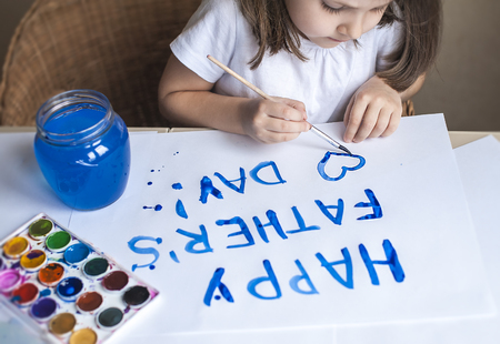 Child making homemade greeting card. Painted hand. A little girl paints a heart on a homemade greeting card as a gift for Father Day. Finger paint. Traditional play concept. Art and craft conceptの写真素材