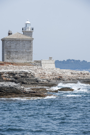 Beautiful historical stone house and tower of white lighthouse on the seashore. Elements voyage. Seascape. Bird flies over the seaの写真素材