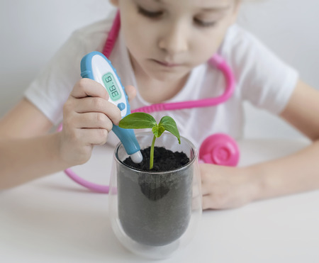 Child hand measuring temperature with thermometer. Experiment on a young plant. Caring for a new life. Climate change. Save earth from global warming. Earth day holiday concept. World Environment Dayの写真素材