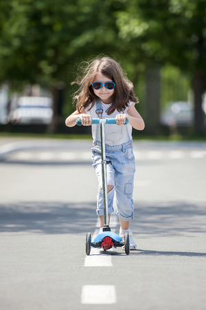 Child riding scooter. Kid on colorful kick board. Active outdoor fun for kids. Summer sports for preschool children. Little happy girl in spring park. The concept of a healthy lifestyleの写真素材