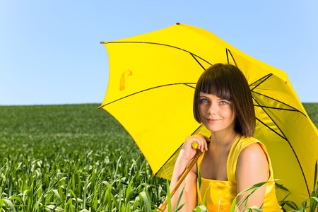 Young  girl with yellow umbrella on a meadow. の写真素材