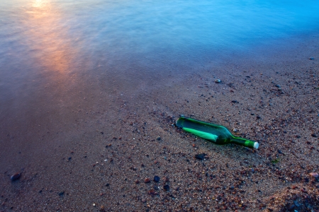 Bottle with the message on sea coast. Long exposure, polarizing filter + ND filter. Movement of waves has blured a background.の写真素材