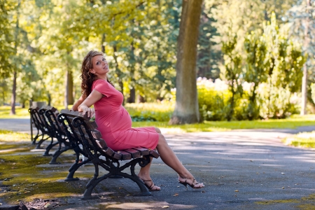 The young pregnant woman has a rest on a bench in parkの写真素材