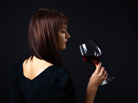 young beautiful woman with red wine on dark backgroundの写真素材