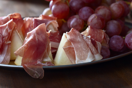 Spanish jamon with melon and grape on a wooden tableの写真素材