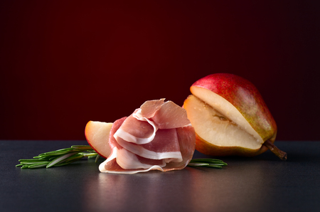Spanish jamon with pear and rosemary on black tableの写真素材