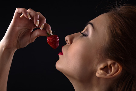 young beautiful woman with strawberry on black backgroundの写真素材