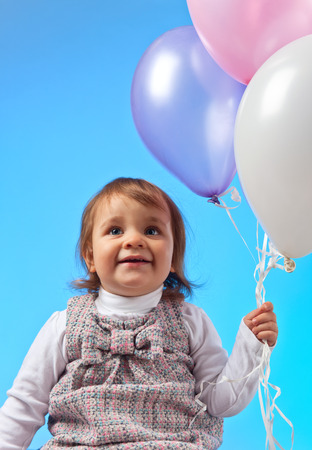 Happy little girl with balloons on a blue backgroundの写真素材