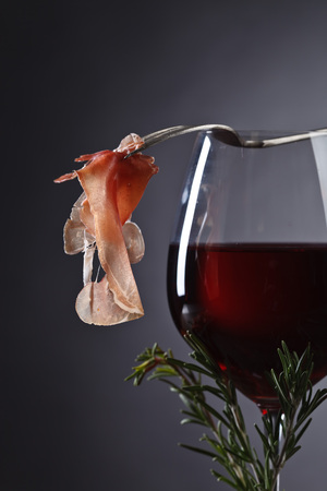Prosciutto with  rosemary and glass of red wine on datk backgroundの写真素材