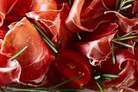 Prosciutto with  rosemary and tomato on a old wooden tableの写真素材