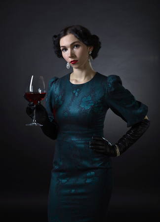 portrait of young beautiful woman in retro style with glass of red wineの写真素材