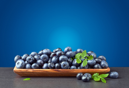 Fresh juicy blueberries with green branch  in wooden dish on a  blue background .  Free space for your text .の写真素材