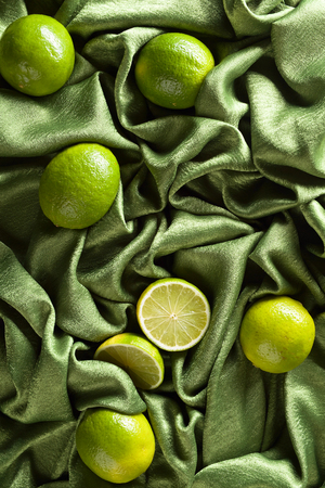 Group of whole and cut fresh limes on a green satin . Top view .の写真素材