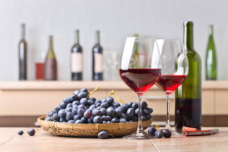 Bottle and glasses of red wine on the kitchen table . Bunch of blue grapes and corkscrew on a  kitchen ceramic table .の写真素材