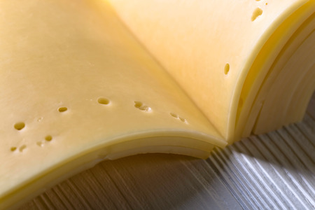 Slices of cheese folded like a book on a white wooden table .