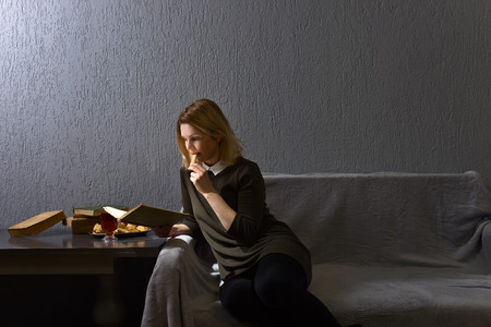 Young woman reading old book . Woman resting with a book on the couch in gray room . Copy space.の写真素材