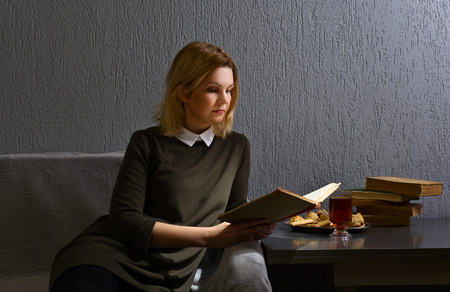 Young woman reading old book . Woman resting with a book on the couch in the gray room . Copy space.の写真素材