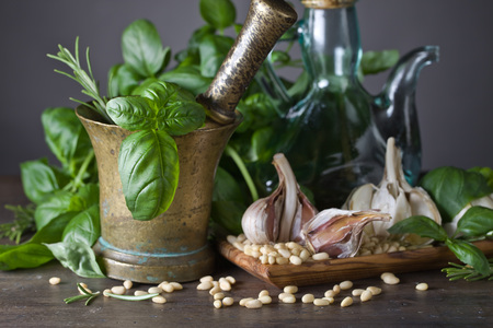 Ingredients for making pesto on a wooden table .Old copper mortar with olive oil, garlic, green basil and  pine nuts .の写真素材