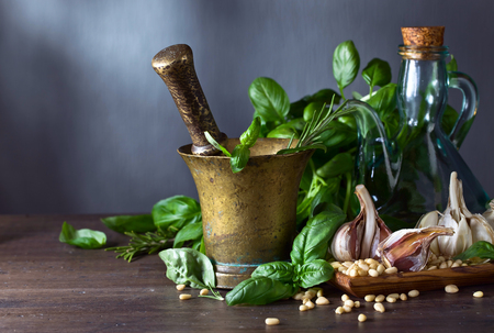 Ingredients for making pesto on a wooden table .Old copper mortar with olive oil, garlic, green basil and  pine nuts .の写真素材