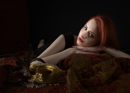 Beautiful redheaded woman in black dress with gold carnival mask.の写真素材