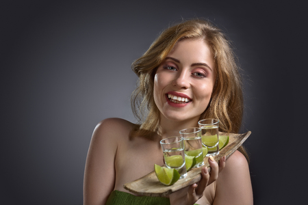 Attractive blonde woman with glasses of tequila and lime in hand . Beautiful professional  makeup and hair .Copy space.の写真素材