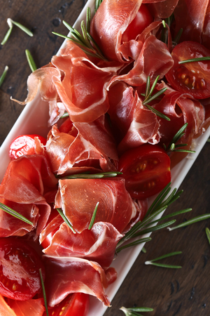 Prosciutto with  rosemary and tomato on a old wooden tableの写真素材