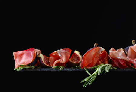 Prosciutto with figs and rosemary on a black background.の写真素材