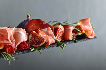 Prosciutto with figs and rosemary on a dark background.の写真素材