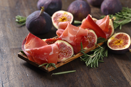Prosciutto with figs and rosemary on a old wooden table.の写真素材
