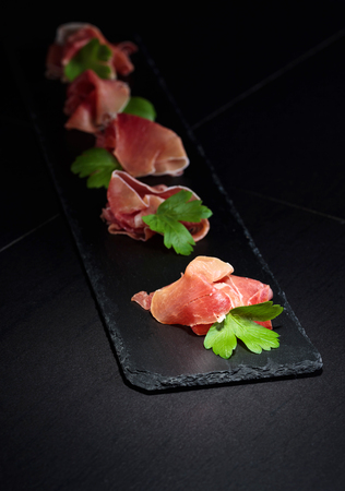 Jamon serrano with parsley on a black table . Healthy organic food . Selective focus .の写真素材