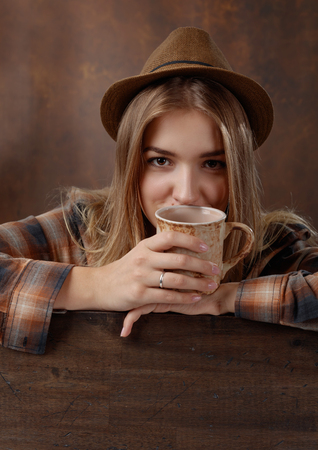 Young beautiful blonde in a brown plaid shirt with a mug of coffee .Natural old wooden background .の写真素材